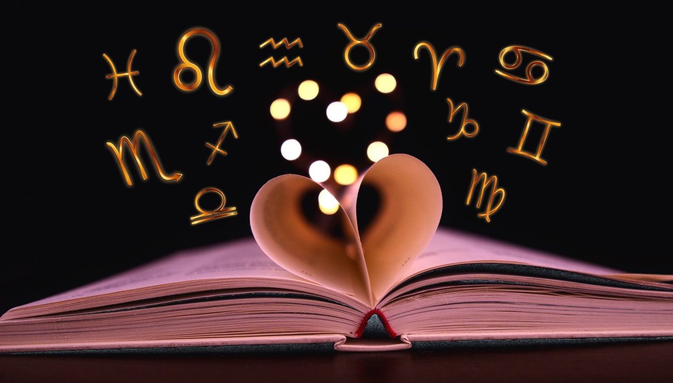 Ein aufgeschlagenes Buch in Herzform mit astrologischen Symbolen darüber.